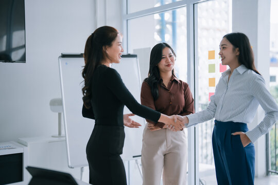 Asian businesswomen making an agreement and shaking hands, feeling happy after a successful partnership meeting in a modern office environment, demonstrating collaboration and teamwork