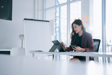 Young Asian businesswoman multitasking in a modern office, using a tablet with a stylus and...