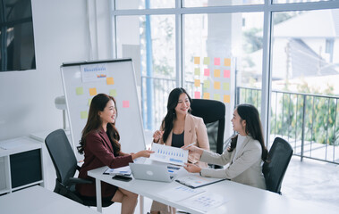 Asian businesswomen are engaging in a corporate meeting, collaborating on project data and discussing financial charts in a bright, contemporary office environment