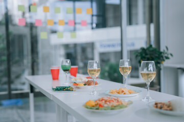 Catering table preparing for an office party, featuring wine glasses, delicious dishes, finger foods, and snacks, setting the scene for a corporate celebration or business gathering