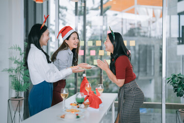 Asian businesswomen celebrating a festive office Christmas party, enjoying food and drinks together, fostering team spirit, and creating happy memories during the holiday season