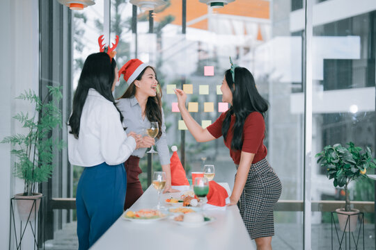 Diverse women colleagues enjoying a festive office Christmas party, laughing and socializing while holding drinks, creating a joyful and celebratory atmosphere