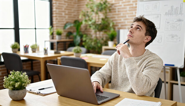 Thoughtful young web designer working on laptop computer in modern office with creative workspace, brainstorming ideas, productivity and innovation concept, casual business environment