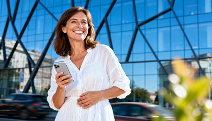 Portrait of a happy mature woman smiling and posing confidently with smartphone in modern casual outfit, lifestyle, positive emotion, technology use, communication concept