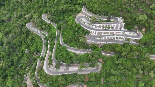 Aerial view of the famous 70 hairpin bends of Kolli Hills, Tamil Nadu. The dizzying road dramatically zigzags up the steep, dense green hillside. Ideal for extreme driving and adventure travel.