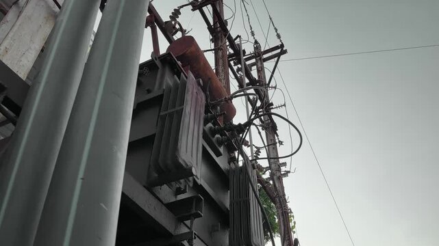 A camera slowly rotates around an old transformer with exposed and tangled electrical wires connected to utility poles. highlighting decaying infrastructure and unsafe wiring