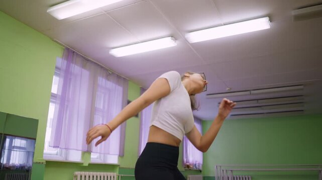 Pretty lady in white top dancing in hall with bright lights above, hair flipping energetically, red lace visible on wrist, movement expressing rhythm, energy and confidence in spacious indoor setting - Powered by Adobe