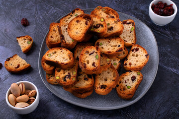 Rusks with dried cranberries and pistachios on ceramic plate on grey table