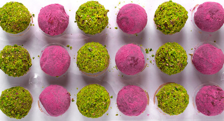 Chocolate candies of two types with sprinkles of ground pistachio and dragon fruit powder in a mold. Making handmade sweets. Top view
