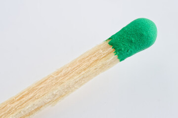 Macro close-up of a wooden match with green sulfur head on white background; concept of ignition, spark, flammable material and fire safety warning. Photo