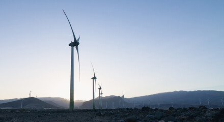 Wide shot at sunset of wind turbines in a desert area with mountains in the background. Renewable energy