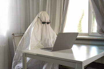 White sheet ghost looking lost at the laptop while working from grey room home office