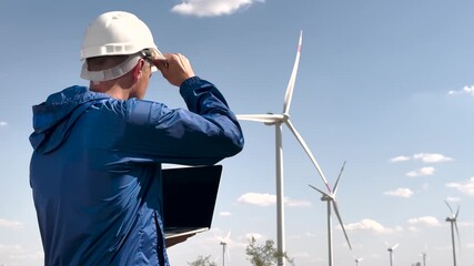 Worker inspects windmill turbine on renewable energy farm. Wind worker ensures efficient turbine operation. Windmill worker monitors turbine performance. Sustainable wind energy worker on field. - Powered by Adobe