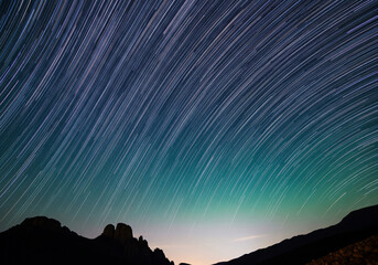 Star trails captured over silhouetted mountains at night, showcasing the mesmerizing movement of celestial bodies across the dark sky
