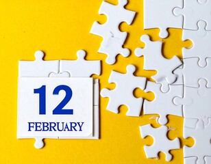 White jigsaw puzzle pieces on a yellow background with the date February 12
