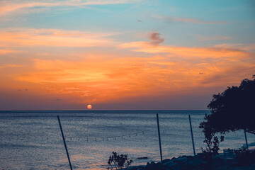 Floating in the waves at sunset, sun just above horizon, going down, orange sky, tranquil sea. Peaceful moment, vacations, summer mood. Dominican Republic. Horizontal video.