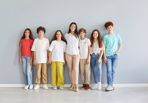 Portrait of a teacher and a group of diverse students stand together against a grey background. The children are happy, smiling, and gathered as a team, symbolizing the joy of togetherness in school.