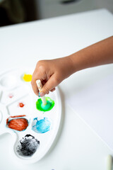 Child painting with colorful palette and brush on white table