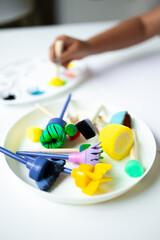 Colorful painting tools on white surface with child hand engaged in art activity