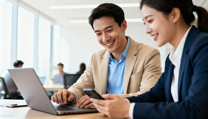 Happy Asian business colleagues working together in a modern office. Smiling man and woman entrepreneurs discussing a project on a laptop, using wireless technology. Teamwork.