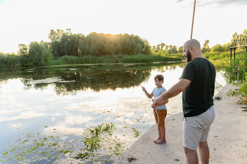 Father and son fishing together at river during sunset