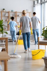 Group of three individuals, two women and one man, engaged in cleaning a modern living room, using a mop and bucket, showcasing teamwork in a bright, spacious environment