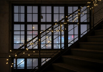 Obraz premium modern interior staircase with string lights leading to large window overlooking city skyline at night