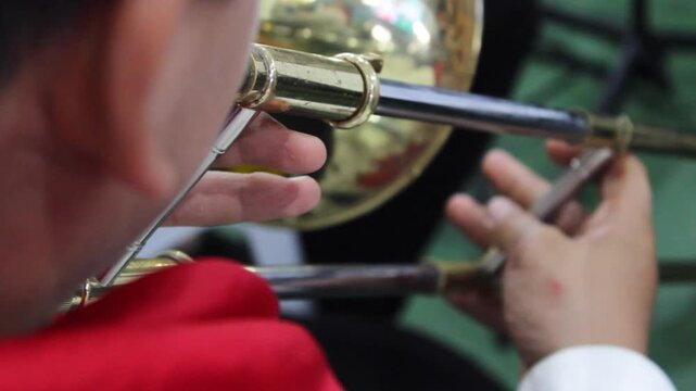 An unrecognizable young man sits while playing a trombone at a public event in Neiva, Huila, Colombia. A concept of Colombian culture and classical music