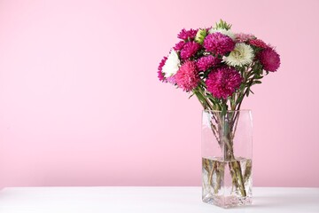 Beautiful flowers in vase on white wooden table against pink background, closeup. Space for text