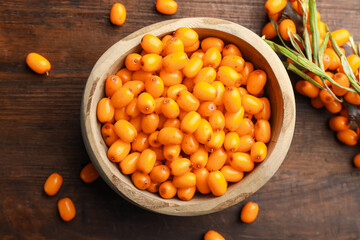 Fresh sea buckthorn berries in bowl and leaves on wooden table, flat lay