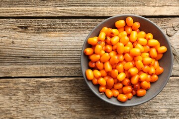 Fresh sea buckthorn berries in bowl on wooden table, top view. Space for text