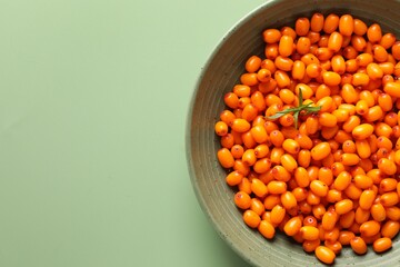 Ripe sea buckthorn berries and leaves in bowl on green background, top view. Space for text