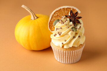 Delicious cupcake with sprinkles, spices, dry orange slice and pumpkin on coral background, closeup. Autumn atmosphere