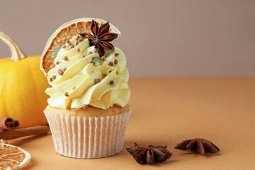 Delicious cupcake with sprinkles, spices, dry orange slice and pumpkin on coral table against background, closeup with space for text. Autumn atmosphere