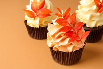 Delicious cupcakes with branches with red leaves on coral background, closeup with space for text. Autumn atmosphere