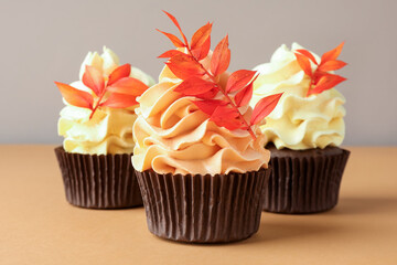Delicious cupcakes with branches with red leaves on coral table against grey background, closeup. Autumn atmosphere