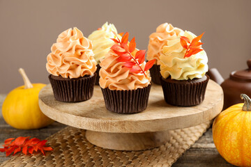 Delicious cupcakes with branches with red leaves on wooden table against grey background, closeup. Autumn atmosphere
