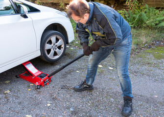 A man jacks up a passenger car for repairs on the street.