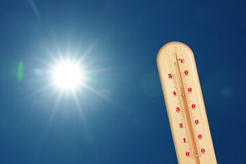 Thermometer showing high temperature against sky with bright sun. Extremely hot weather