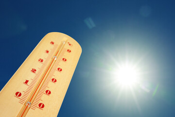 Thermometer showing high temperature against sky with bright sun. Extremely hot weather