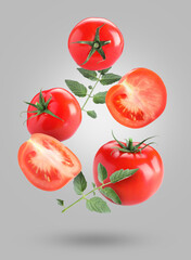 Fresh ripe tomatoes and green leaves falling against grey background