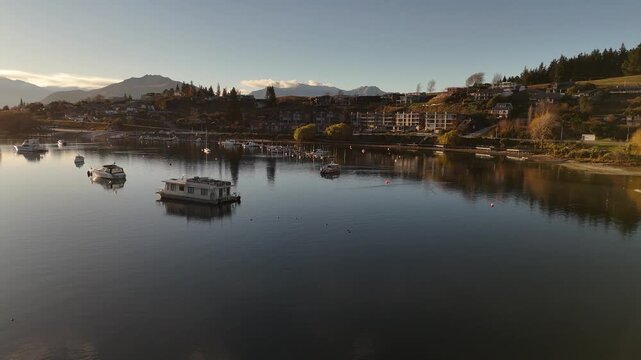 Low flight over wanaka lake in new Beamen during sunset time. Anchored boats and luxury waterfront apartments in New Zealand.