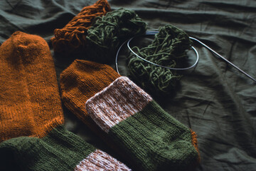 Cozy knitted socks with yarn ball and knitting needles. Striped wool socks on dark green sheet....
