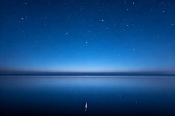 Starlit night sky reflected over calm water with a distant light on the horizon
