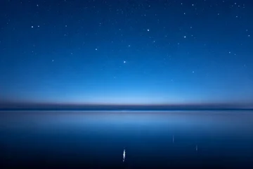 Tableau sur plexiglas Réflexion Starlit night sky reflected over calm water with a distant light on the horizon  © 九地 之下