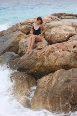 Beautiful woman wearing stylish swimsuit on rocks at beach