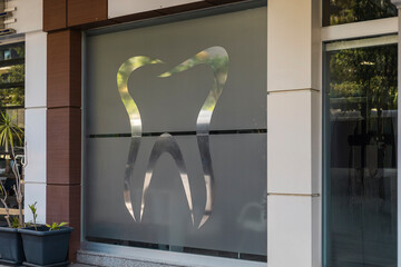A large tooth symbol is displayed on a frosted glass window of a dental clinic in a bustling city. Bright sunlight illuminates the surroundings, attracting attention from passersby