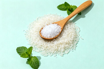 White rice grains with a wooden spoon and mint leaves on a light blue background