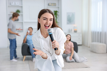 Fototapeta premium Young woman singing karaoke with friends at home, selective focus