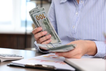 Fototapeta premium Woman counting dollar banknotes at table, closeup